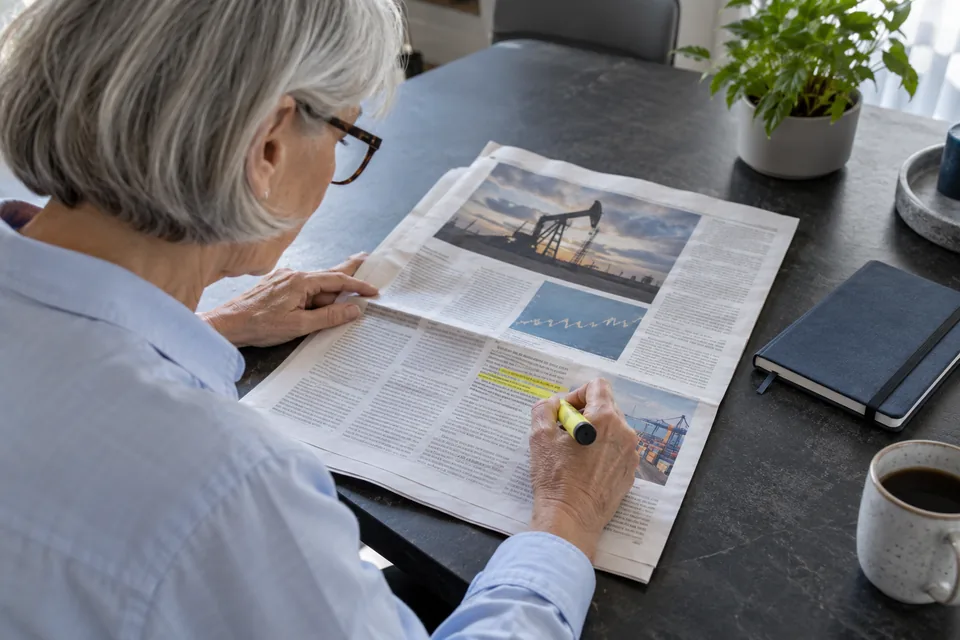 Persoon markeert een passage in een krant, met een gesloten notitieboek ernaast.
