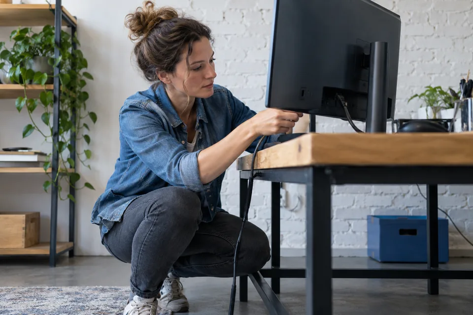 Persoon controleert de aansluiting van een beeldscherm op een werkbank.