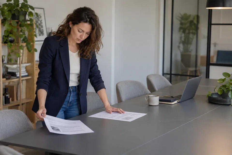 Persoon vergelijkt twee documenten op een lange werktafel.